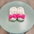 White crochet baby booties with pink bow.