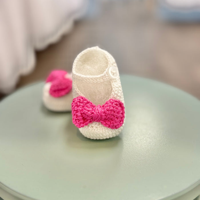 White crochet baby booties with pink bow.