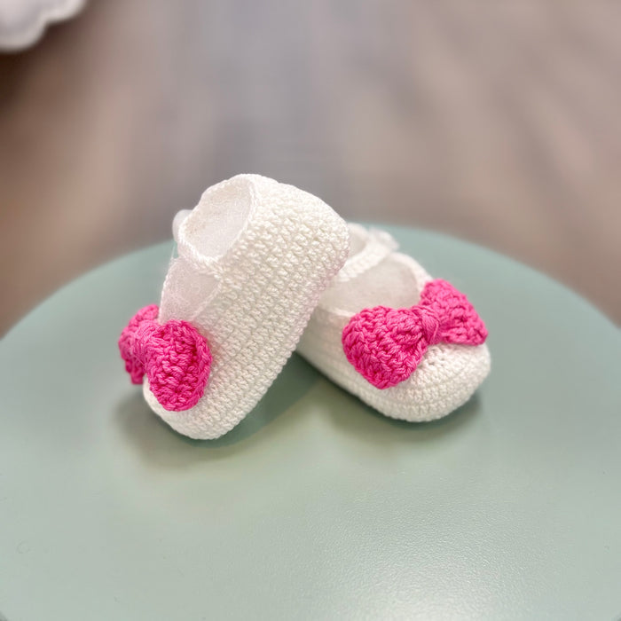 White crochet baby booties with pink bow.