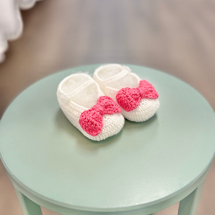 White crochet baby booties with pink bow.