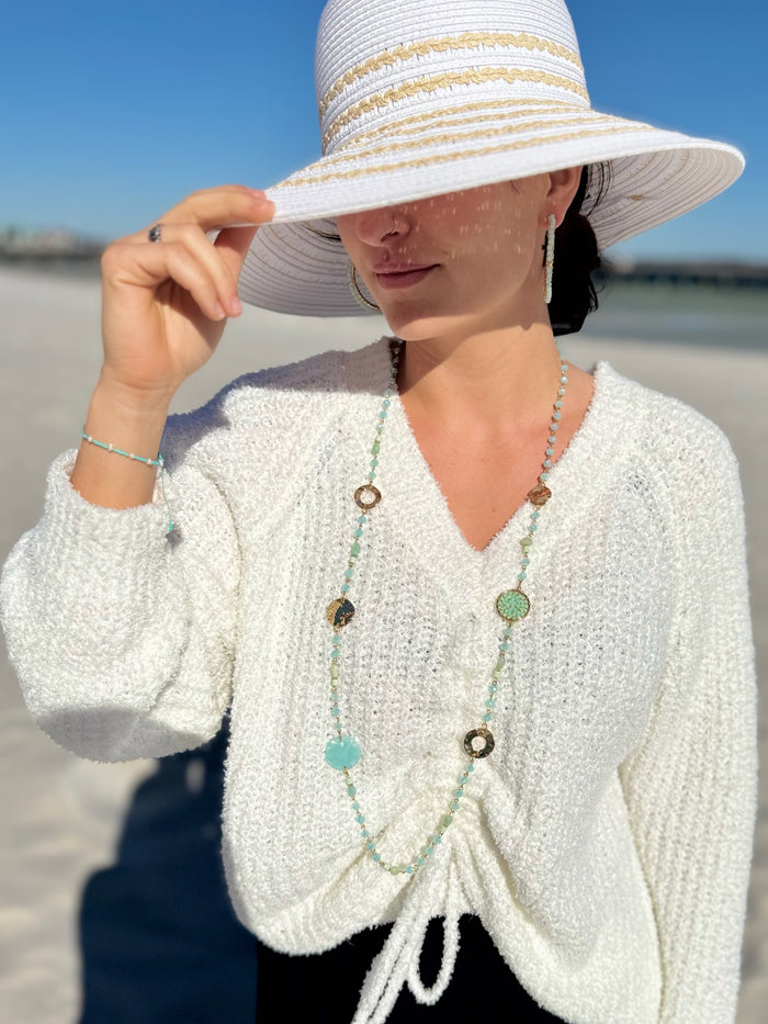 Woman wearing a white knit cardigan and sun hat on a beach