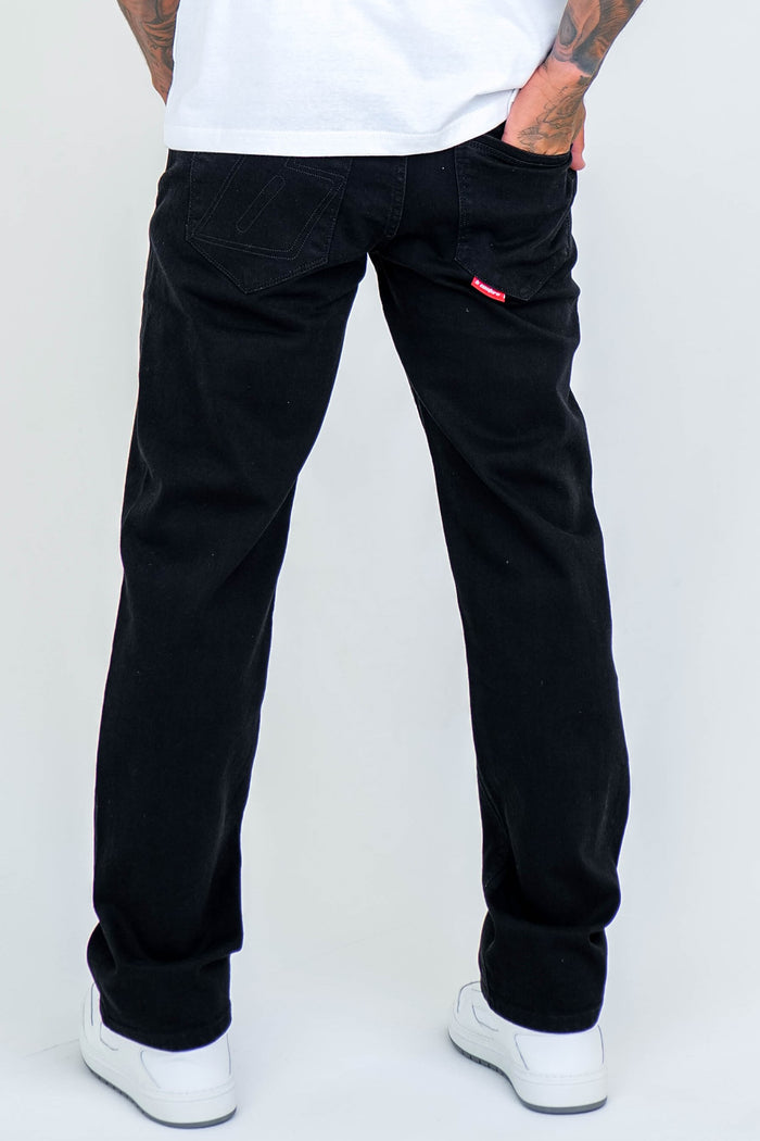 A person stands facing away from the camera, hands on hips, showcasing the back of their Beckenham Straight Fit Stretch Denim Jeans in Black against a plain white background. White sneakers complete the look.