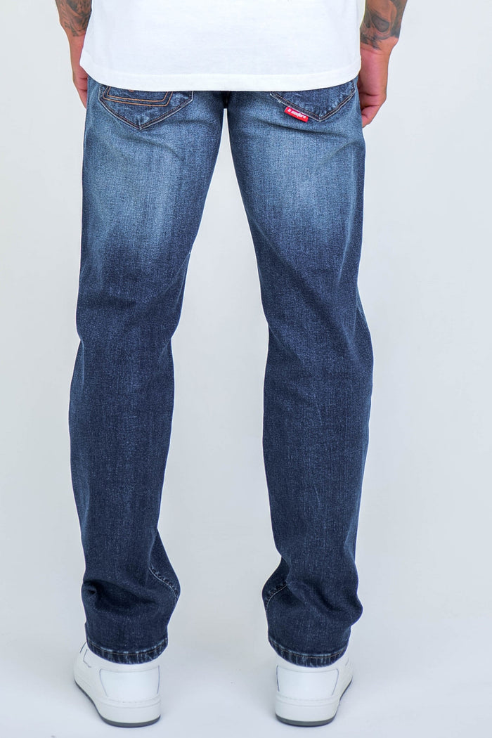 A person faces away, wearing B Couture Beckenham Straight Fit Stretch Denim Jeans in dark blue with a faded effect and back pocket stitching, paired with white sneakers and a crisp white shirt for a comfortable, stylish look.