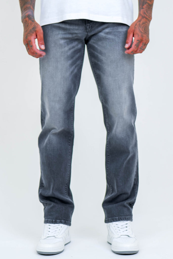 A person wearing B Couture Beckenham Straight Fit Stretch Denim Jeans in grey and white sneakers stands with arms at their sides against a plain light background, showing only the lower half of their body.