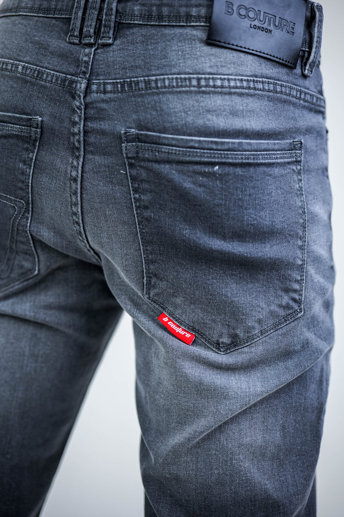 Close-up of the back of a person wearing B Couture Beckenham Straight Fit Stretch Denim Jeans in grey, featuring two back pockets, a red tag on the right pocket, and a black leather B Couture patch on the waistband.