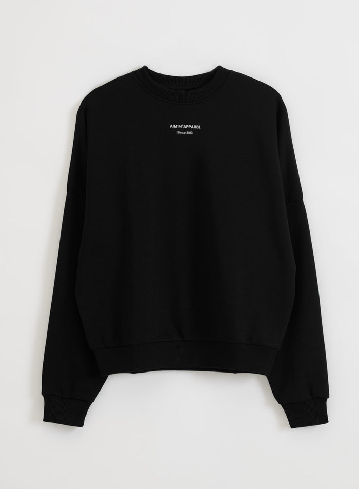 Rento musta terry-sweatshirt hopeisella aim'n-logolla ja resoreilla kuvattuna tasokuvana.