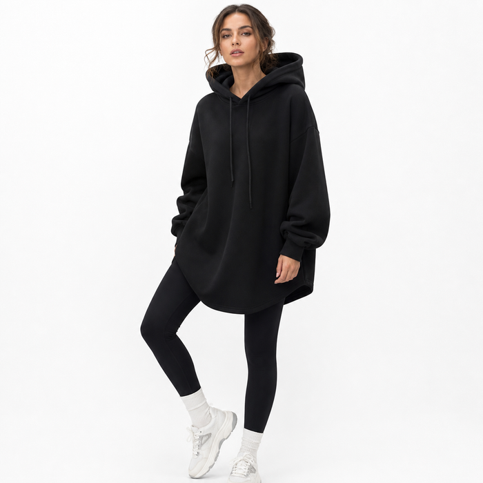 Black oversized hoodie women styled with fitted pants, showing longline silhouette, hood and relaxed drop shoulders in front.