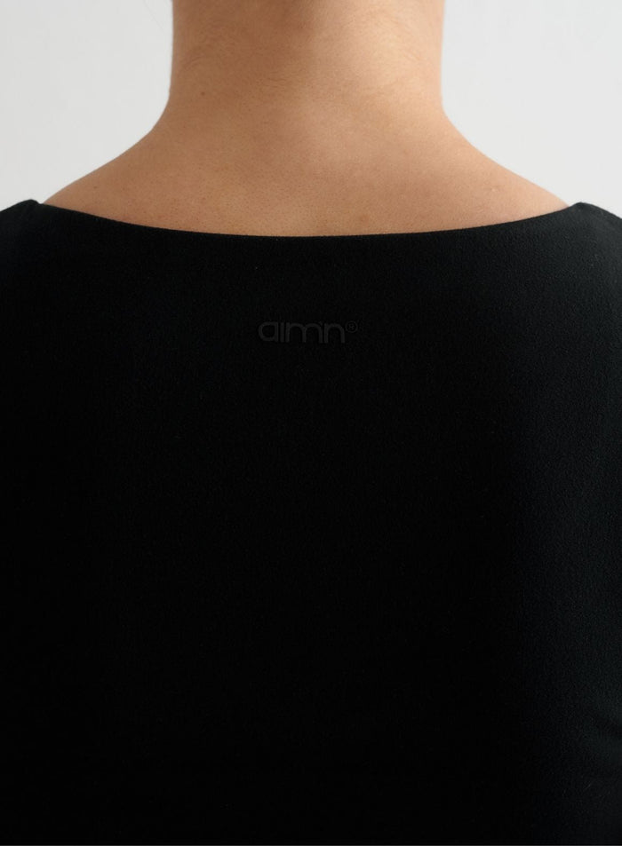 Musta lyhythihainen Sense-bralette, jossa on hienovarainen kuminen aim'n-logo pehmeässä harjatussa selkäosassa.