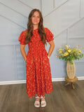 Girl wearing tea length red floral dress with smocked bodice.