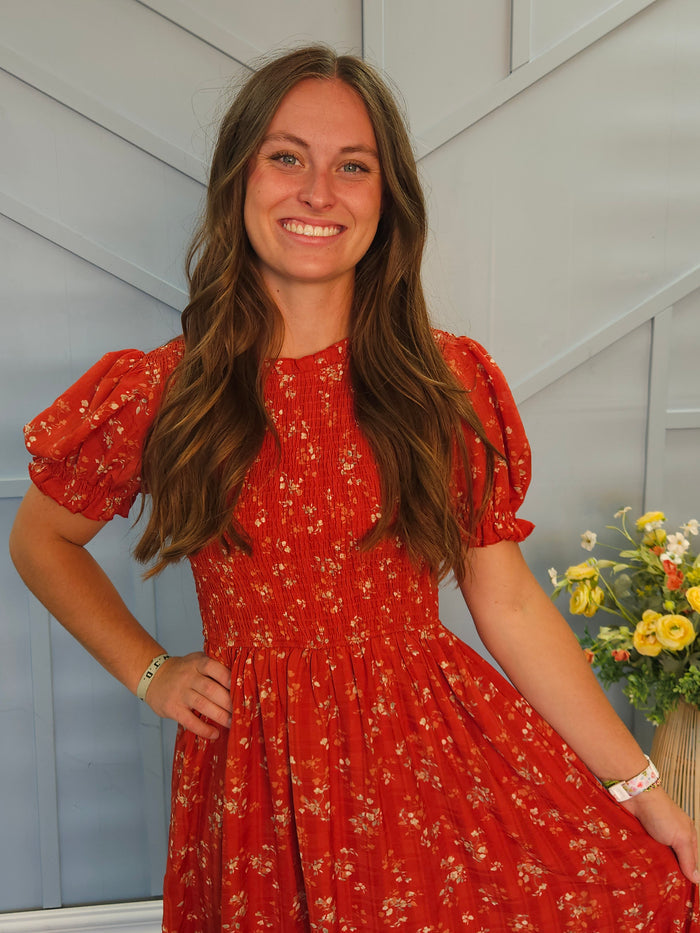 Girl wearing tea length red floral dress with smocked bodice.