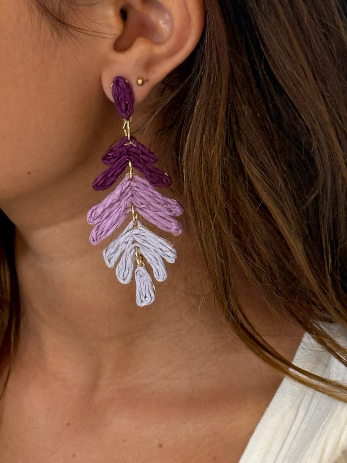 A pair of purple ombre cascading leaf earrings with gold accents on a model