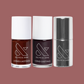 Three Olive and June nail polish bottles in rich brown, deep purple, and silver finish on muted mauve background