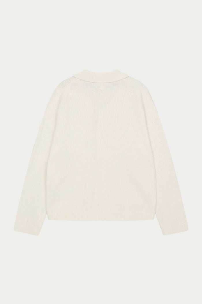 A long-sleeved off white shirt with a ribbed revere collar and crochet knit fabric against a white background.