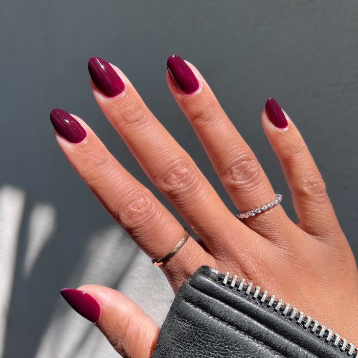 Hand with warm medium skin tone wearing Luxe Loafer gel polish in deep crimson jelly for a shiny, long-lasting manicure outdoors