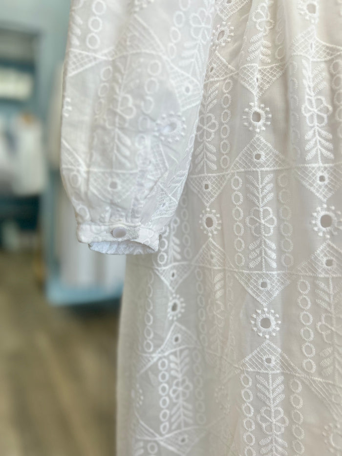 White eyelet dress with bishop sleeves and button cuffs.
