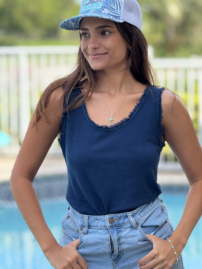 A woman wearing a navy tank top with a ruffled raw edge detail and blue jeans, standing by a pool.