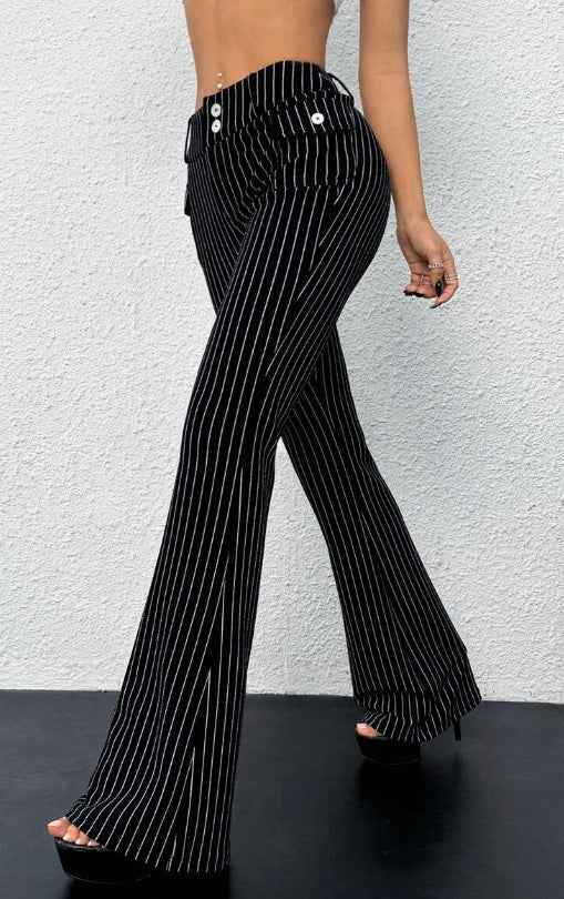 Black pinstripe pants worn by a person against a white textured wall.