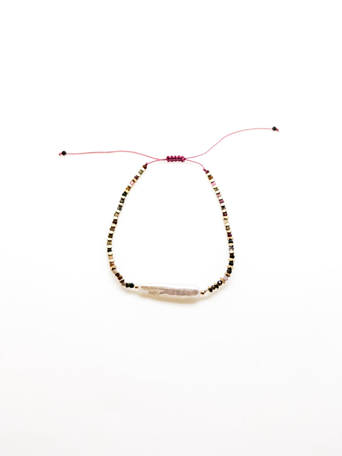 A purple bracelet with a baroque-style pearl and earthy-toned beads, featuring a sliding knot closure.