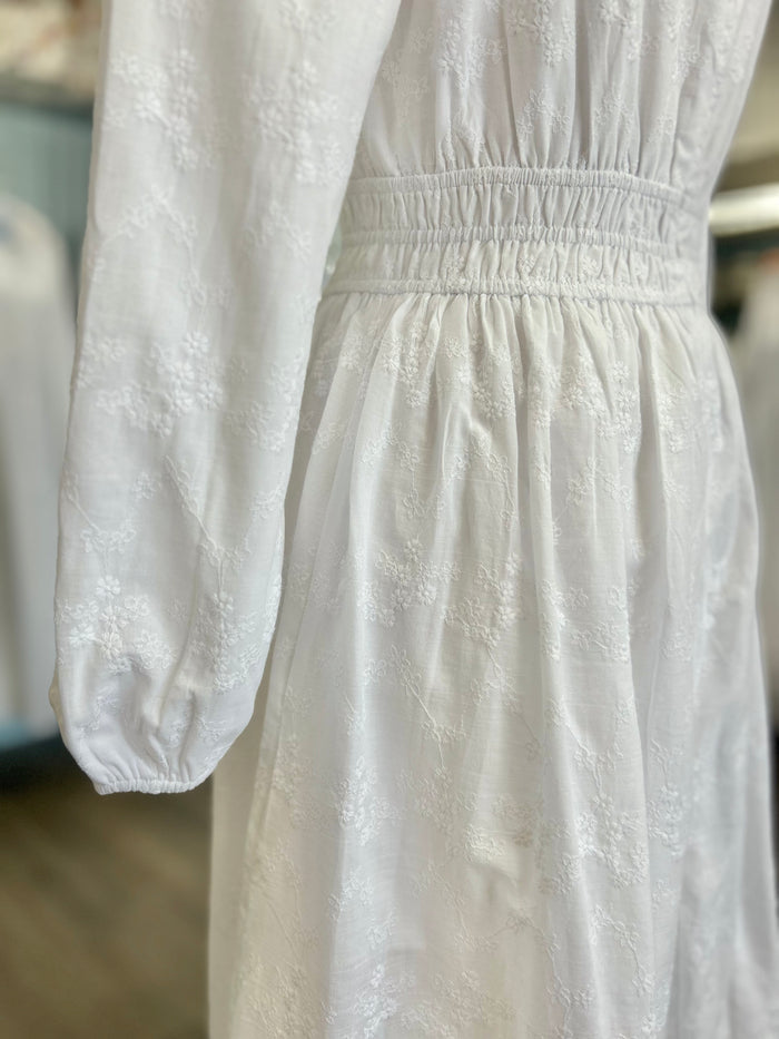 White embroidered dress with cinched waist and bishop sleeves.
