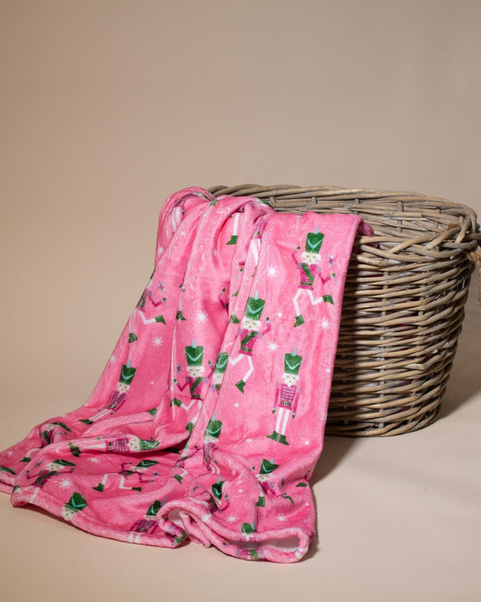 Pink and green nutcracker patterned throw draped over a wicker basket