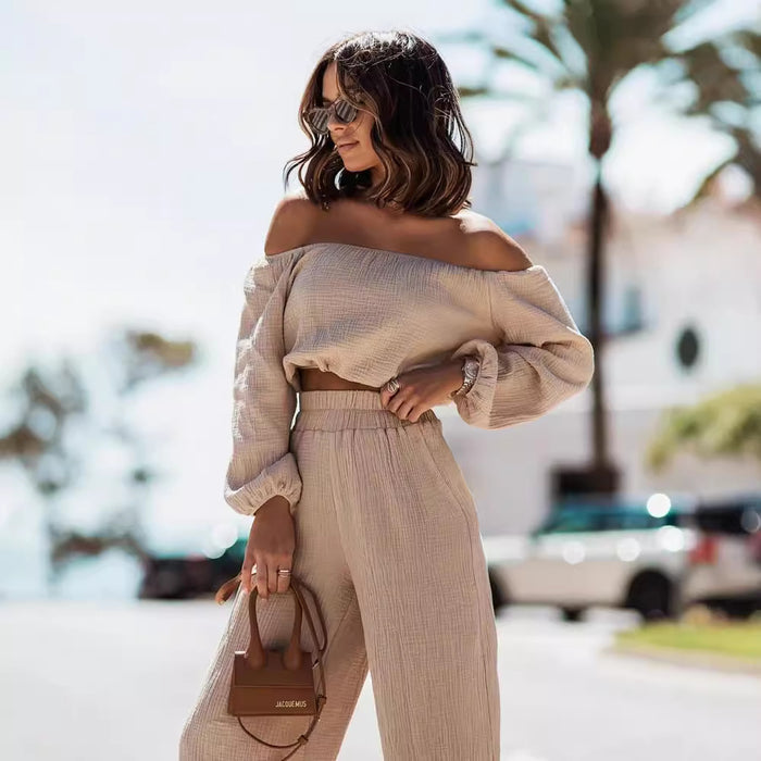 Woman in beige off-shoulder top and pants holding a brown handbag outdoors.