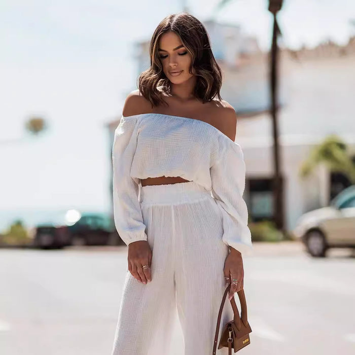 Woman wearing a white off-shoulder top and pants with a blurred street background