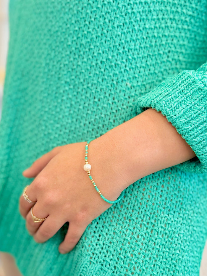 Person wearing a turquoise bracelet and ring on a matching teal sweater.