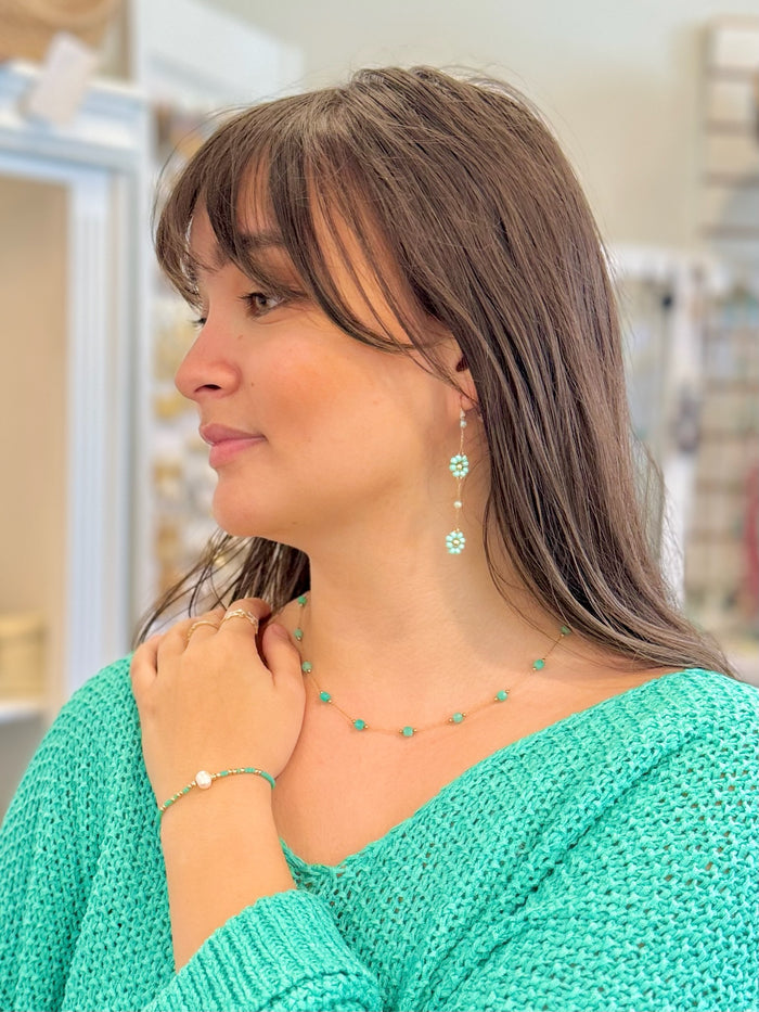 Woman wearing a green knitted sweater and turquoise jewelry in an indoor setting