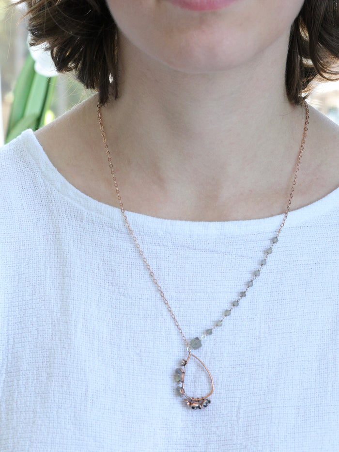 Woman wearing a Rose gold teardrop necklace with labradorite gemstones and asymmetrical chain, handcrafted by Nina Halls for Ardor Boutique.
