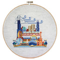 Cross-stitch of Chicago landmarks including the Willis Tower and Ferris wheel, framed in a wooden hoop.