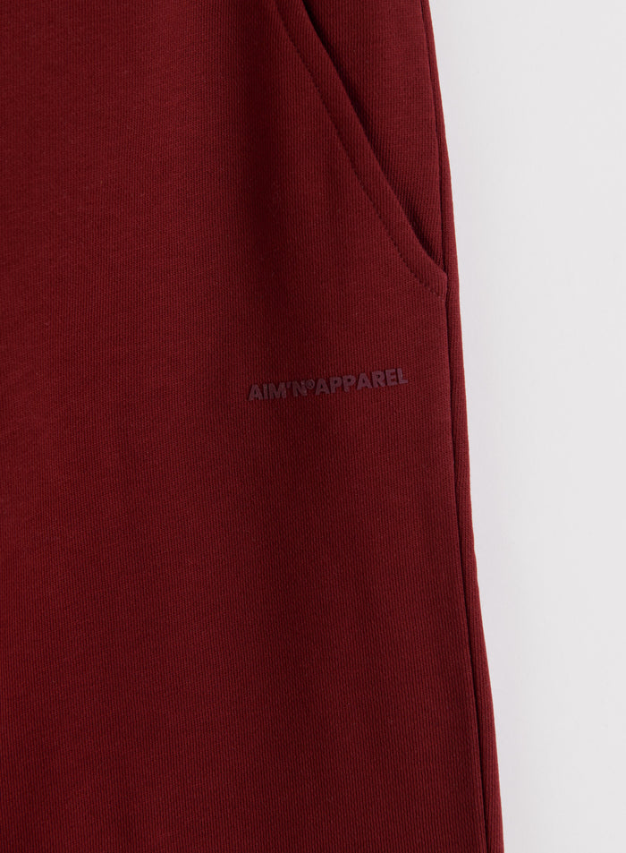 Lähikuva ruby-punaisista Chunky Terry Sweatpants -housuista, joissa on sivutasku ja hienovarainen aim'n-logo.