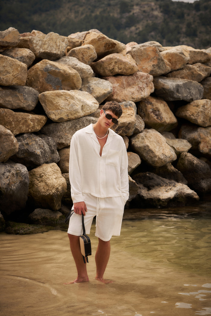 Man in white outfit standing in water near a stone wall