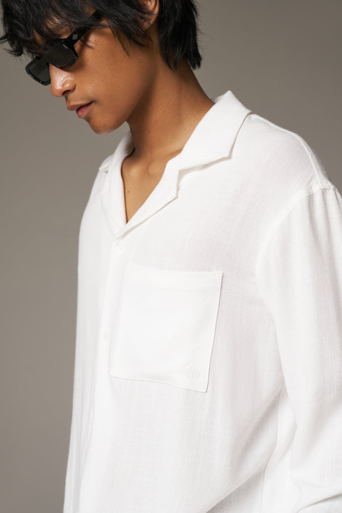 Close image of a man wearing a long sleeved white shirt and sunglasses against a neutral background.