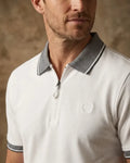 Man wearing a white polo shirt with a patterned collar against a beige background