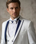 Man wearing a white suit with blue lapels and a bow tie against a neutral background