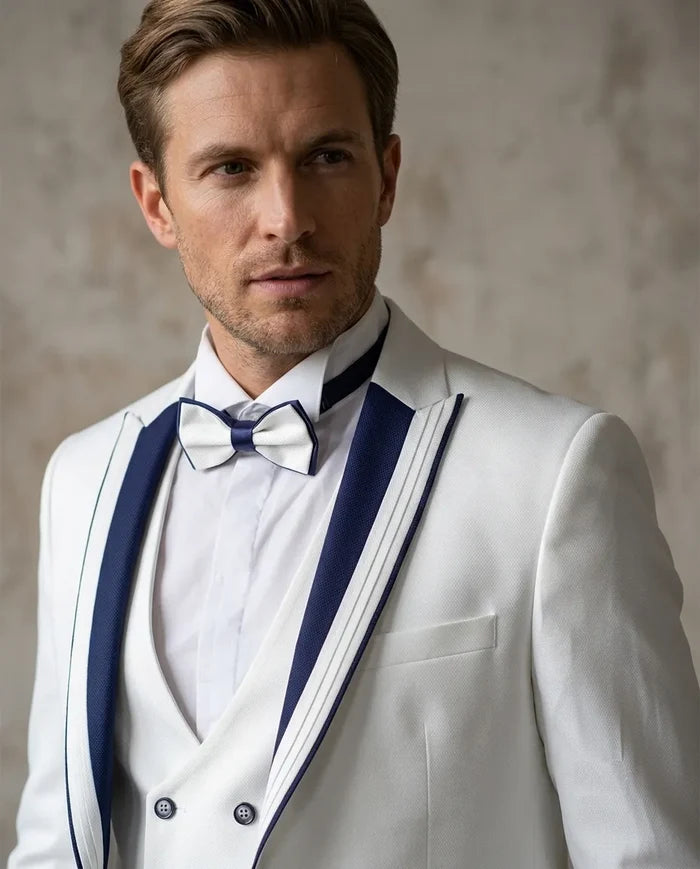 Man wearing a white suit with blue lapels and a bow tie against a neutral background