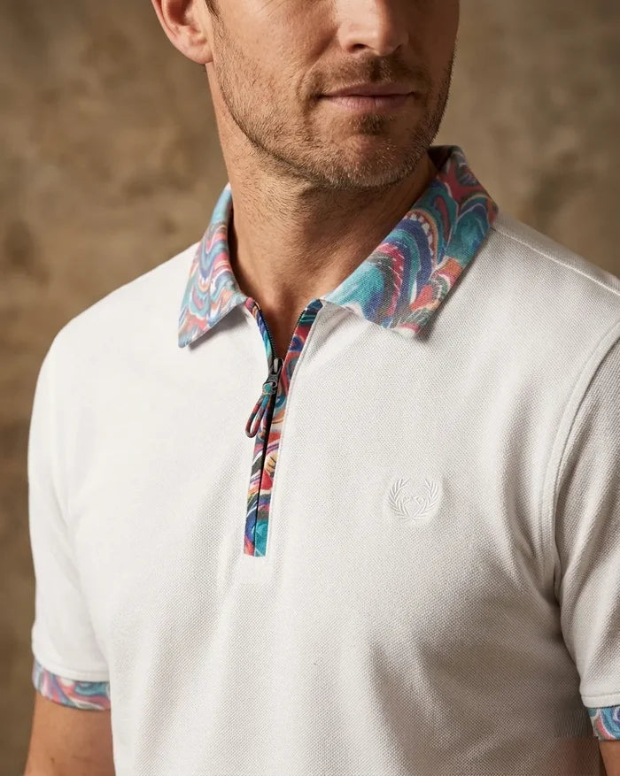 Man wearing a white polo shirt with a colorful patterned collar and cuffs against a brown background