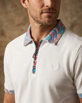 Man wearing a white polo shirt with a colorful patterned collar and cuffs against a brown background