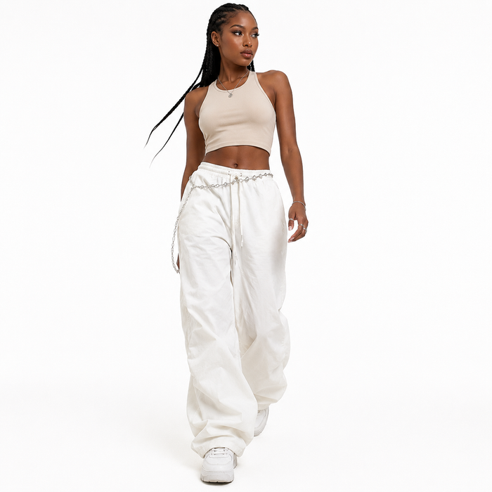 A woman modeling a two-piece outfit consisting of a beige ribbed crop top and white baggy sweatpants with a silver chain detail at the waist, set against a plain white studio background.