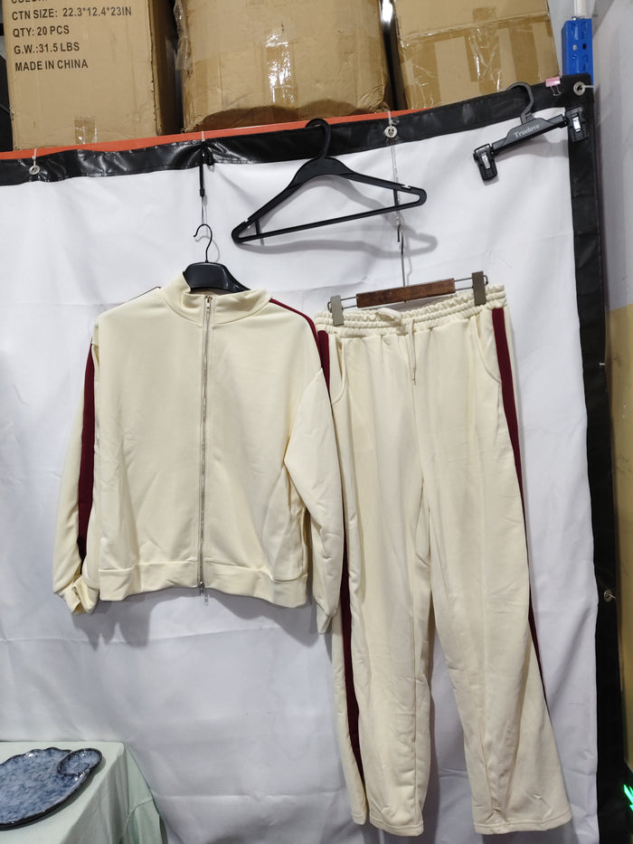 Beige tracksuit hanging on a rack against a white backdrop with cardboard boxes in the background.